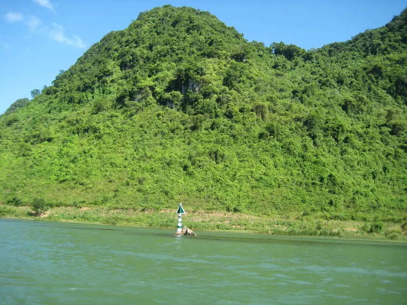 Núi đá vôi xanh mướt nhô lên bên dòng sông với cột tiêu dẫn đường ở Phong Nha.