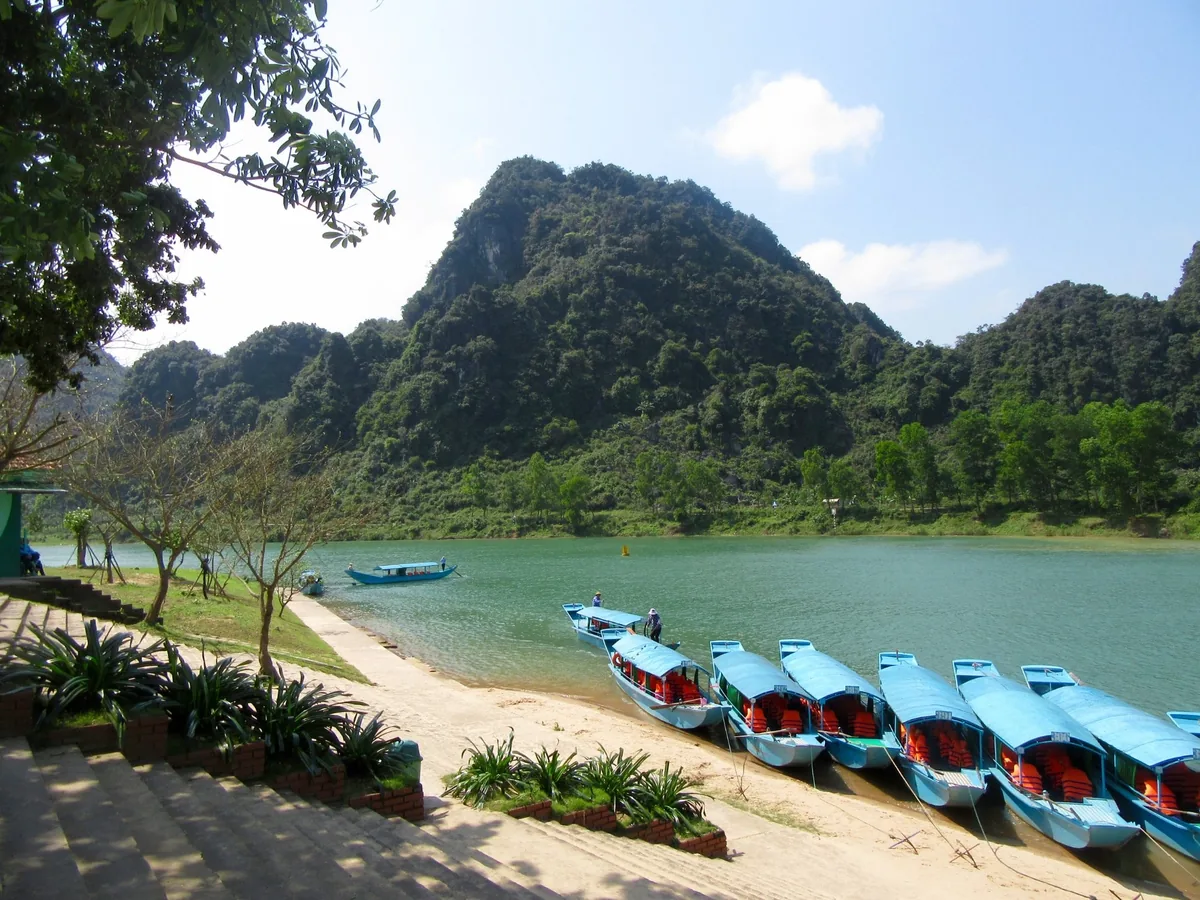 Những chiếc thuyền du lịch màu xanh đậu bên bờ sông dưới núi đá vôi gần động Phong Nha.
