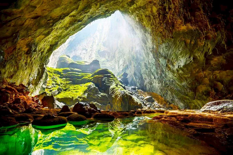 Ánh nắng chiếu vào một hang động đá vôi rộng lớn với hồ nước xanh và đá rêu phong ở miền Trung Việt Nam.