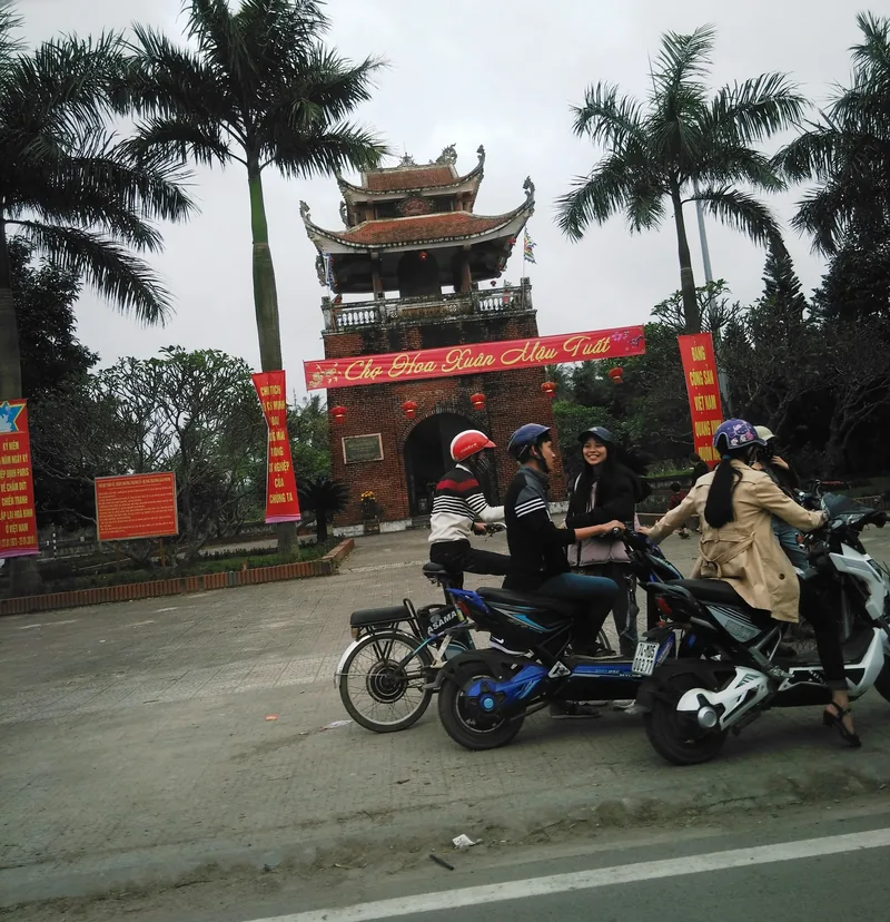Những người đi xe máy dừng trước cổng thành gạch của Thành cổ Quảng Trị được trang trí băng rôn lễ hội đỏ.