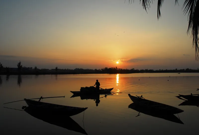 Một người chèo thuyền lướt qua sông Hiếu Giang tĩnh lặng lúc hoàng hôn gần Quảng Trị, in bóng trên nền trời vàng.