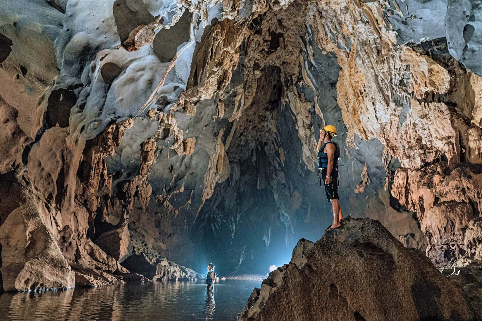 Những người khám phá đội mũ bảo hộ và áo phao dạo bước trong hang đá vôi rộng lớn có sông ngầm ở Quảng Bình.