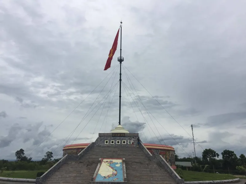 Cột cờ cao với lá cờ Việt Nam vươn lên trên đài tưởng niệm đá tại khu DMZ gần Huế.