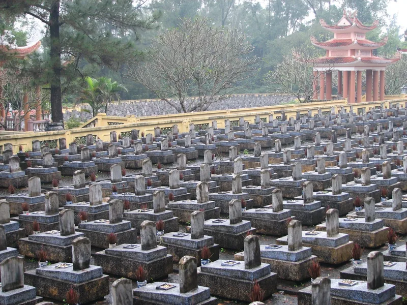 Hàng dãy mộ bia đồng nhất trải rộng tại Nghĩa trang Liệt sĩ Quốc gia Trường Sơn với nhà bia đỏ phía sau.