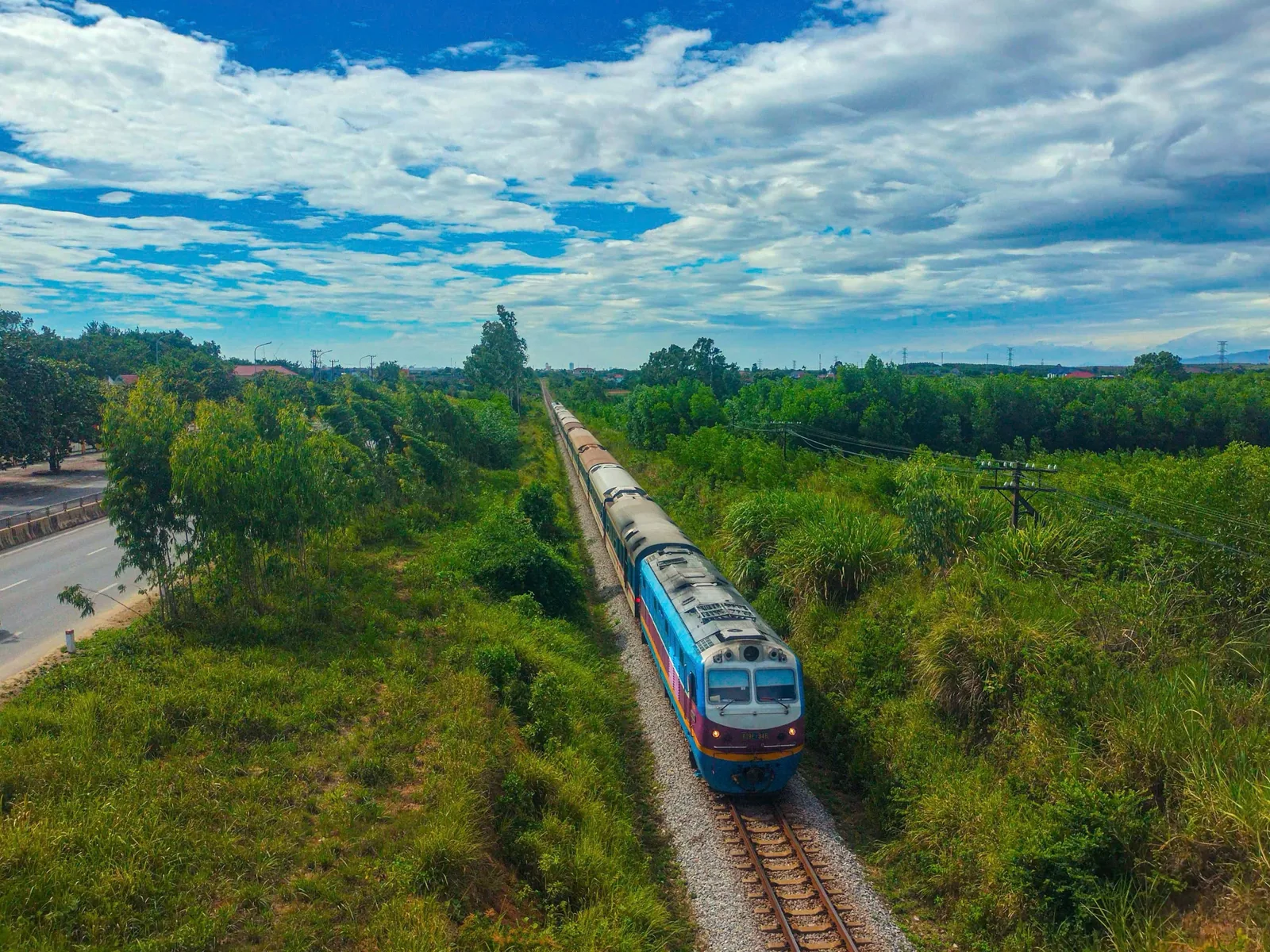 Đoàn tàu khách chạy trên đường ray xuyên qua vùng quê xanh mướt gần khu vực DMZ Quảng Trị dưới bầu trời xanh.