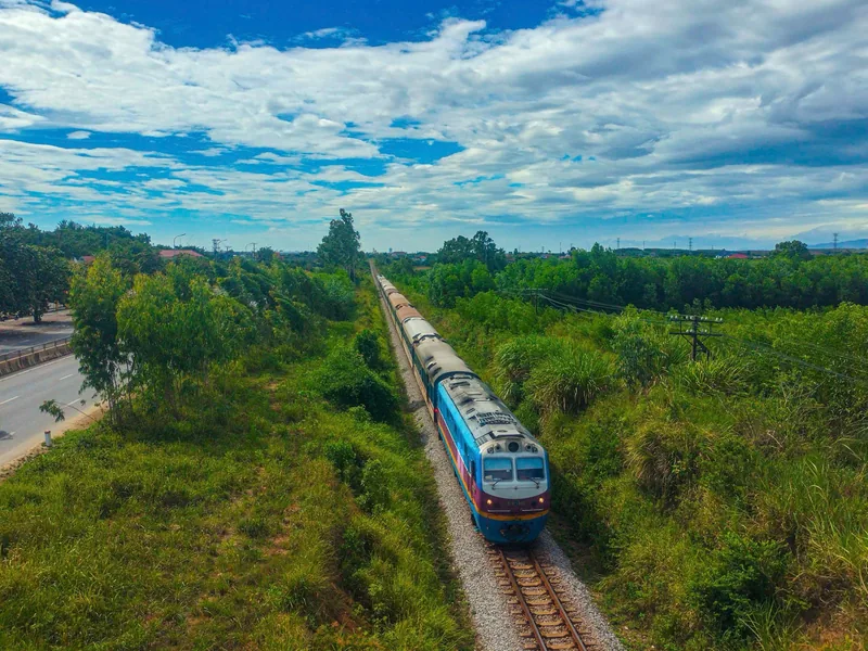 Đoàn tàu khách chạy trên đường ray xuyên qua vùng quê xanh mướt gần khu vực DMZ Quảng Trị dưới bầu trời xanh.