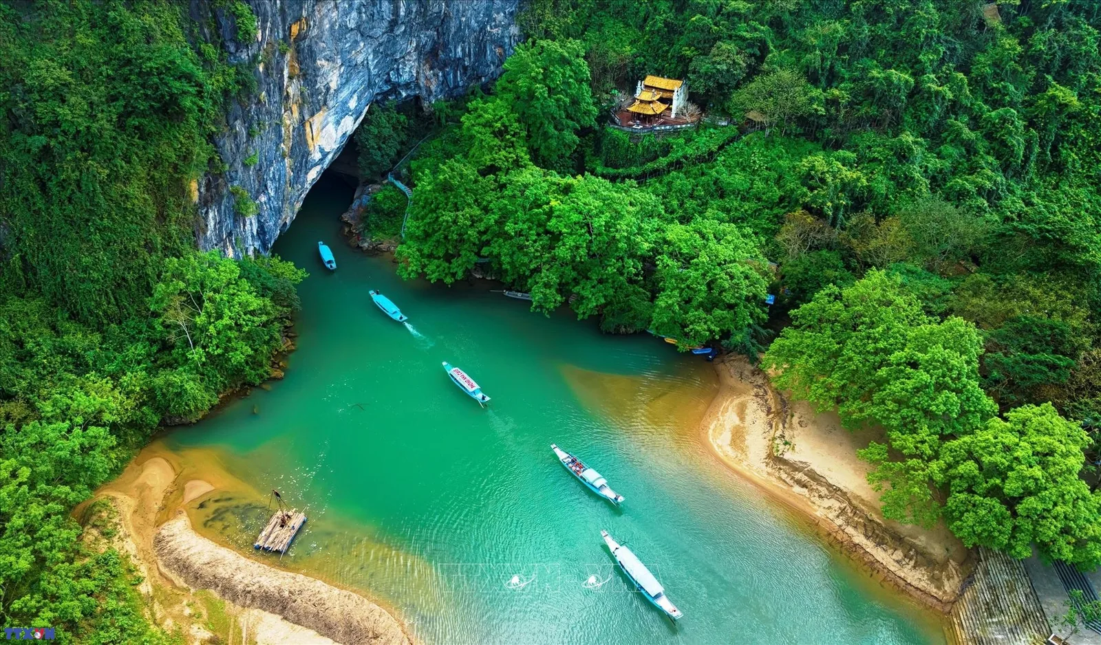 Toàn cảnh từ trên cao những chiếc thuyền lướt trên dòng nước xanh ngọc dẫn vào cửa hang Phong Nha giữa rừng núi đá vôi xanh.