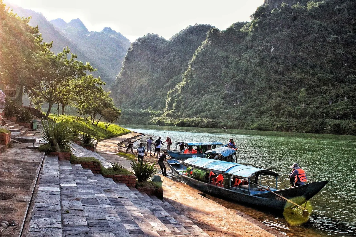 Du khách lên thuyền gỗ dọc bờ sông dưới những dãy núi đá vôi gần động Phong Nha.