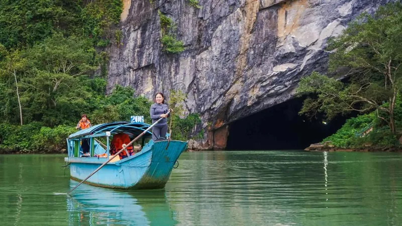 Người phụ nữ chèo thuyền màu xanh tiến vào cửa hang đá vôi trên dòng sông xanh ở Phong Nha.